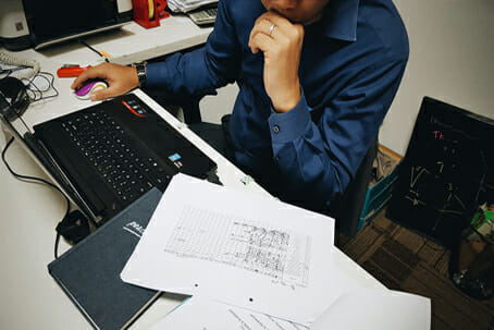 Man in blue shirt looking at spreadsheets while on computer